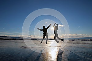 Silhouettes of happy young people jumping over the ice of lake Baikal at sunset.