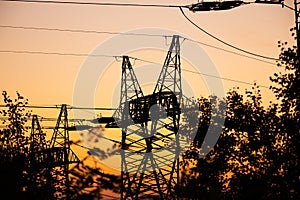Silhouettes of high voltage pylons against the orange sky during sunset.