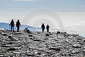 Silhouettes of hikers coming down from the top of Mulhacen with a sea of low clouds in the background photo