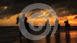 Silhouettes of the horse riders on the beach at sunset.