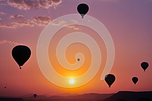 Silhouettes of hot air balloons flying above rocky landscape during sunrise