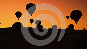 Silhouettes of hot air balloons on orange sunset sky background.