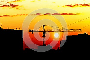 Silhouettes of houses and construction crane against setting sun, city skyline at sunset