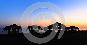 Silhouettes of hovels with the roofs covered with palm leaves for rest on the beach at sunset