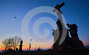 Silhouettes of kids flying kites with stone christianity monument in the foreground at sunset