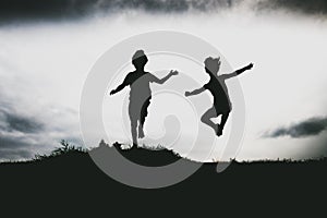 Silhouettes of kids jumping from a sand cliff at the beach