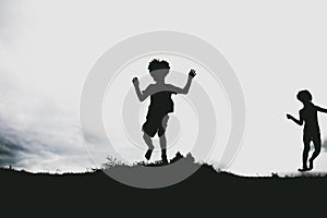 Silhouettes of kids jumping from a sand cliff at the beach