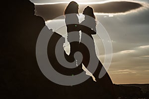Silhouettes of love couple man and woman at rock mountain in beautiful nature sunset. Couple love concept. Shadow