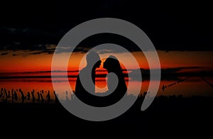 Silhouettes of lovers couple hugging at sunset, sunrise against the backdrop of the sea, sun, clouds in fiery red, orange colors