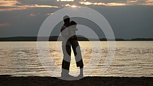 Silhouettes of lovers at sunset. Young beautiful couple embracing on a shore of the lake