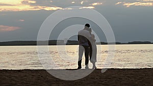 Silhouettes of lovers at sunset. Young beautiful couple embracing on a shore of the lake