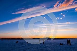 Silhouettes of male fishermen on winter fishing on the ice of the river