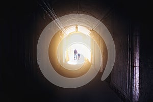 Silhouettes of man and child, father and daughter, walking into light from dark tunnel