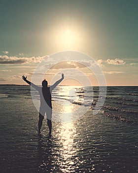 Silhouettes of a man with open arms sunbathing on the seashore and facing the sun setting down. Summer and travel concepts. Retro