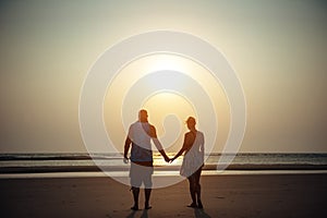 Silhouettes of man and woman on the background of the sea in the rays of setting sun. Young couple in love holding hands at sunset