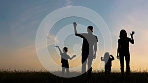 Silhouettes of man, woman, boy and girl at sunset. Dad, mom, son and daughter wave their hands at the hello camera and