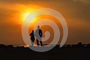 Silhouettes of man and woman on a dais stand with their backs and look at sea sunset