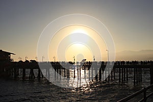 Silhouettes of many unrecognizable people walking across the Santa Monica Pier at a slightly foggy sunset