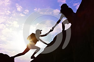 Silhouettes of man and woman helping each other to climb on hill photo