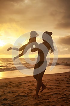 Silhouettes of mother and little girl daughter playing fun on beach at sunset sky background