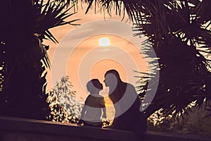 Silhouettes of mother and son, who meet the sunset in the tropics against the backdrop of palm trees