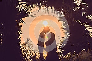 Silhouettes of mother and son, who meet the sunset in the tropics against the backdrop of palm trees