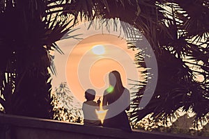 Silhouettes of mother and son, who meet the sunset in the tropics against the backdrop of palm trees