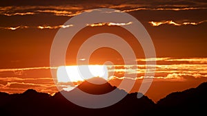 Silhouettes of mountains in golden sunset. Moving clouds in orange sky.