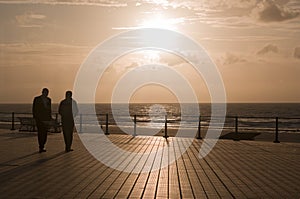 silhouettes of a pair of male friends walking along the terrace in the sunset