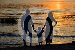 Silhouettes of parents and child on the background of the setting sun