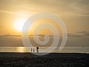 Silhouettes of people against the backdrop of a bright sunset. Orange sunset. Family on vacation. Sea