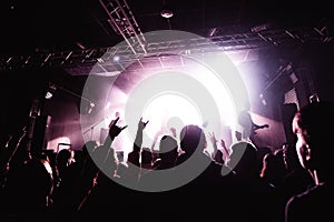 Silhouettes of people in a bright in the pop rock concert in front of the stage. Hands with gesture Horns. That rocks. Party in a