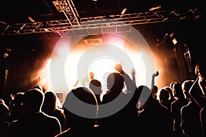 Silhouettes of people in a bright in the pop rock concert in front of the stage. Hands with gesture Horns. That rocks. Party in a