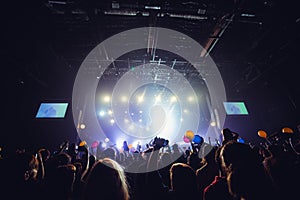 Silhouettes of people in a bright in the pop rock concert in front of the stage. Hands with gesture Horns. That rocks. Party in a