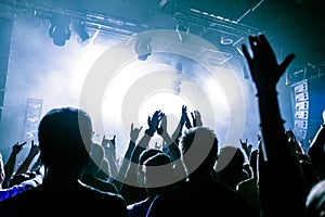 Silhouettes of people in a bright in the pop rock concert in front of the stage. Hands with gesture Horns. That rocks. Party in a