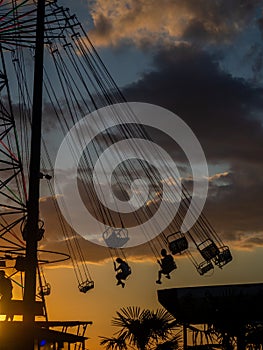 Silhouettes of people on the carousel. Concept of fun and entertainment. People on carousels at sunset. Resort town. Adrenalin.