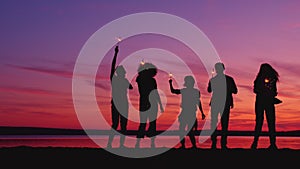 Silhouettes of people dancing with bengal lights on the beach at night having fun