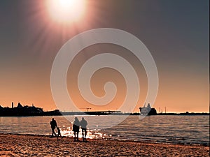 Silhouettes of people and  family couple  walking  on the beach sand at sunset on sea on horizon ship in harbor ,reflection of sun