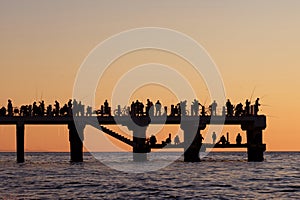 Silhouettes of the people fishing and enjoying the sunset over sea