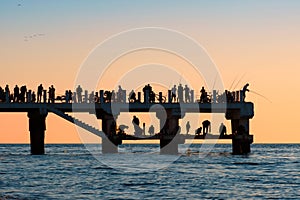Silhouettes of the people fishing and enjoying the sunset on a pier