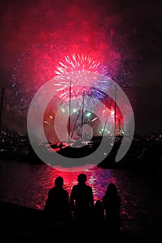 Silhouettes of people at harbor by fireworks night scene