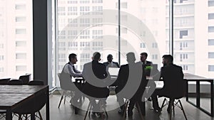 Silhouettes of people sitting at the table. A team of young businessmen working and communicating together in an office