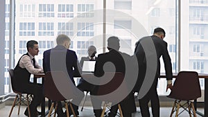 Silhouettes of people sitting at the table. A team of young businessmen working and communicating together in an office