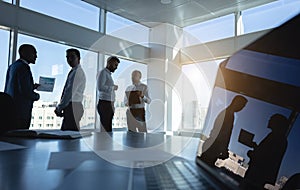 Silhouettes of people standing near a panoramic window in a modern office. Team of young professional business people