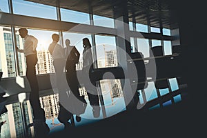 Silhouettes of people standing near a panoramic window in a modern office. Team of young professional business people