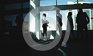 Silhouettes of people standing near a panoramic window in a modern office. Team of young professional business people