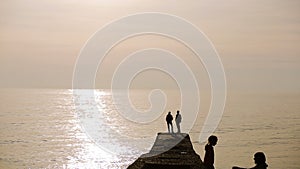 Silhouettes of people standing on a pier at sunset by the sea, couple in love,