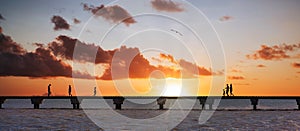 Silhouettes of people walking on a bridge at sunset