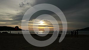 Silhouettes of people walking on the summer beach at sunset