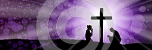 Silhouettes of praying woman and man under the cross in purple color